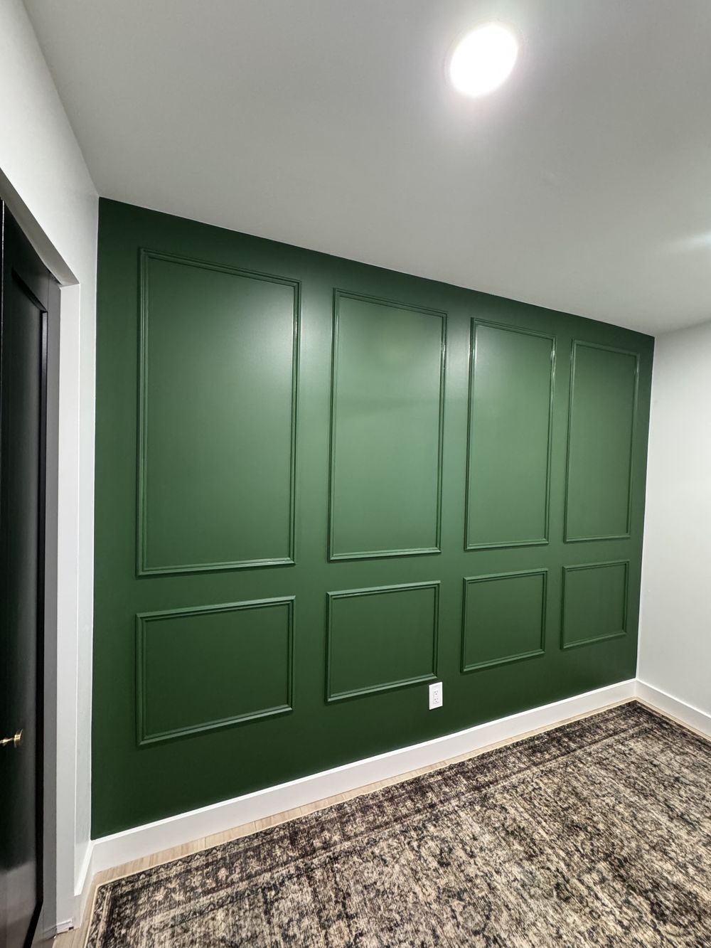 Deep green accent wall with applied box moulding and crisp white baseboard in a Phoenix home