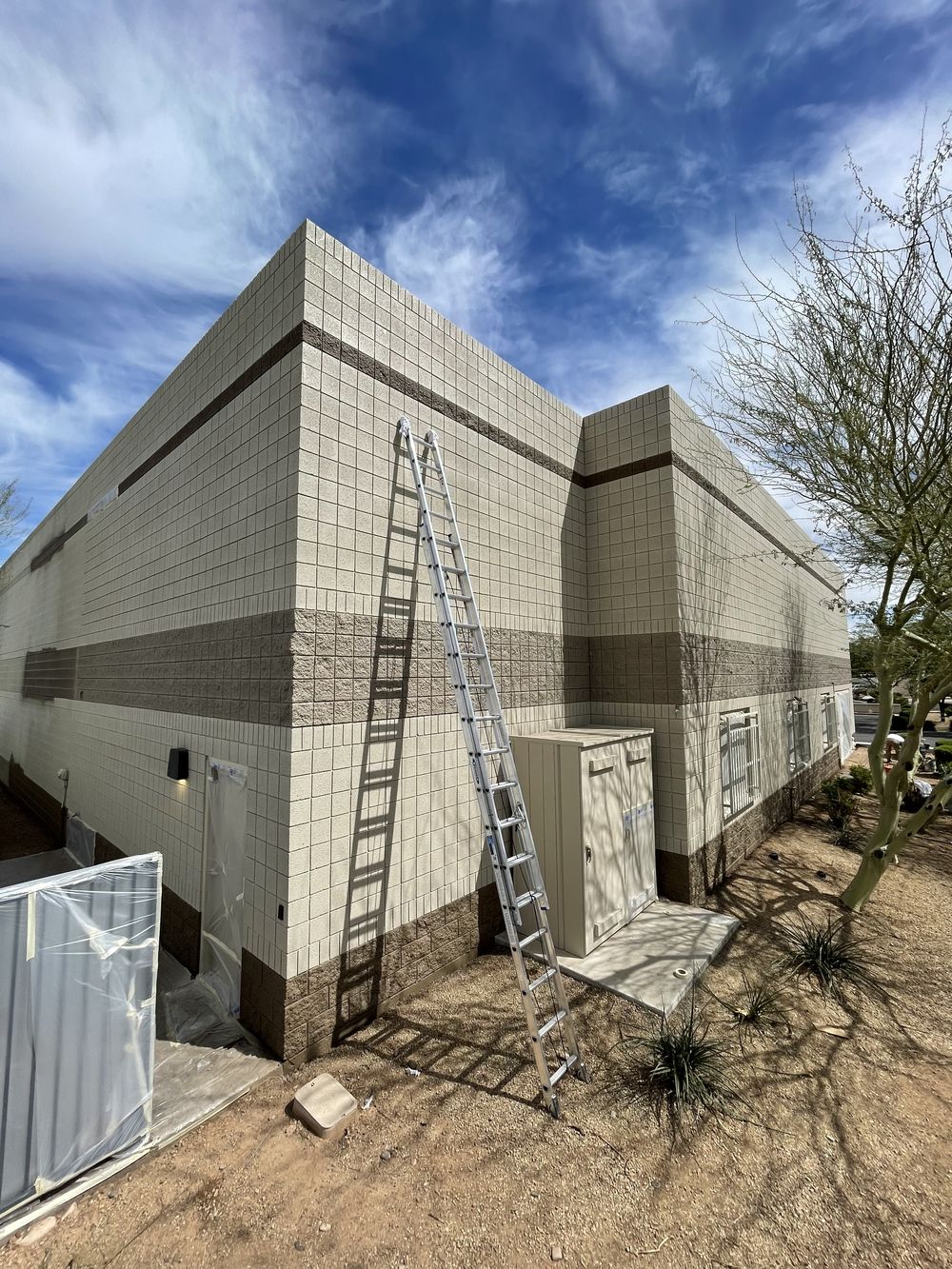 Extension ladder against a multi-unit Arizona block building prepped for exterior repaint