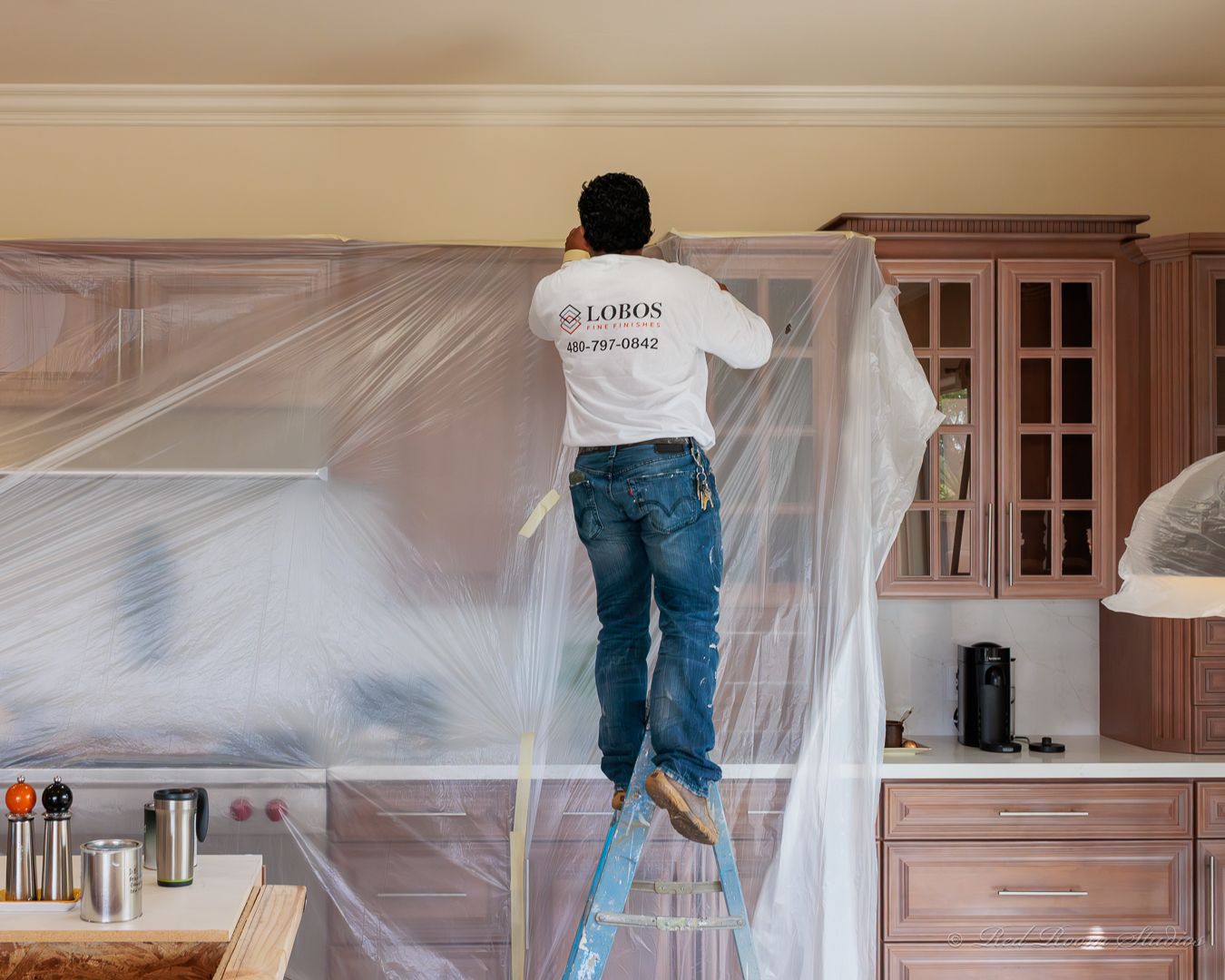 A LOBOS painter masking upper cabinets with plastic sheeting before spraying