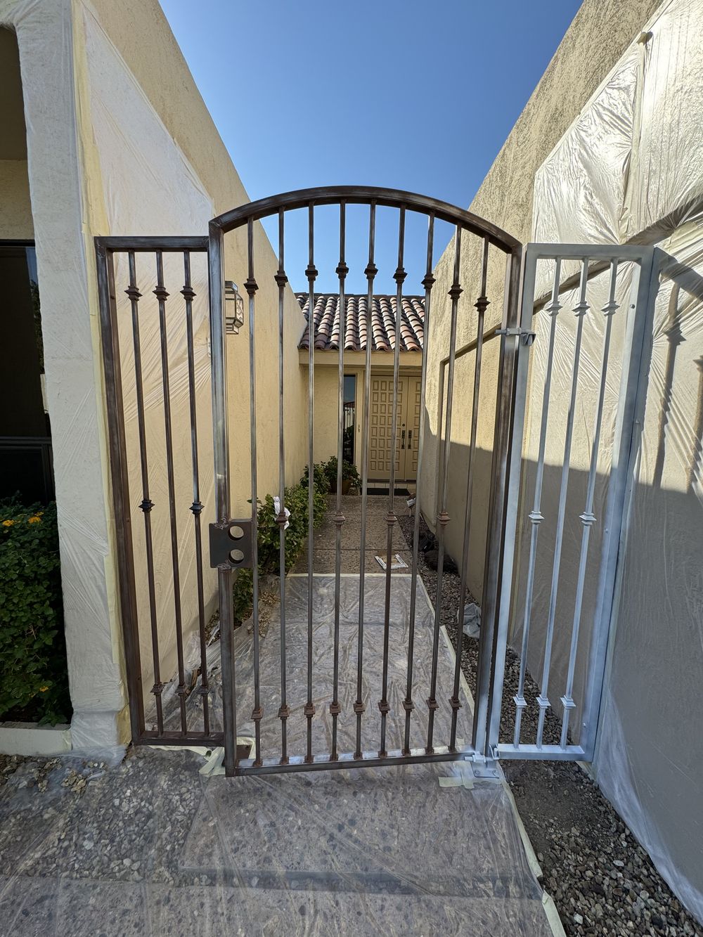 Wrought iron gate before refinishing, rusted with the surrounding walls masked off