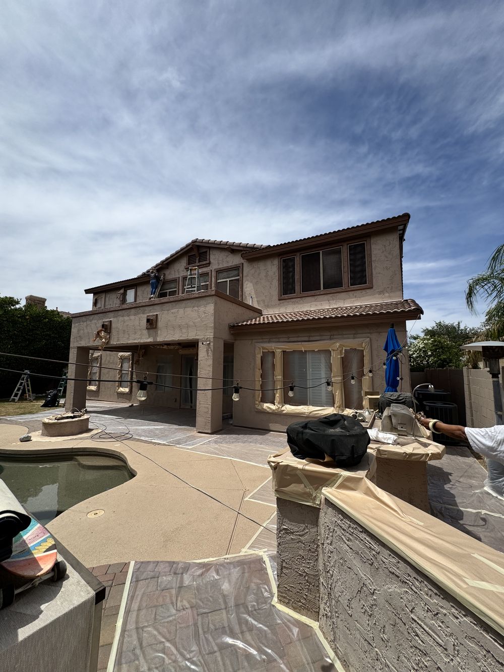Chandler two-storey home being repainted around a pool with patio furniture masked and protected