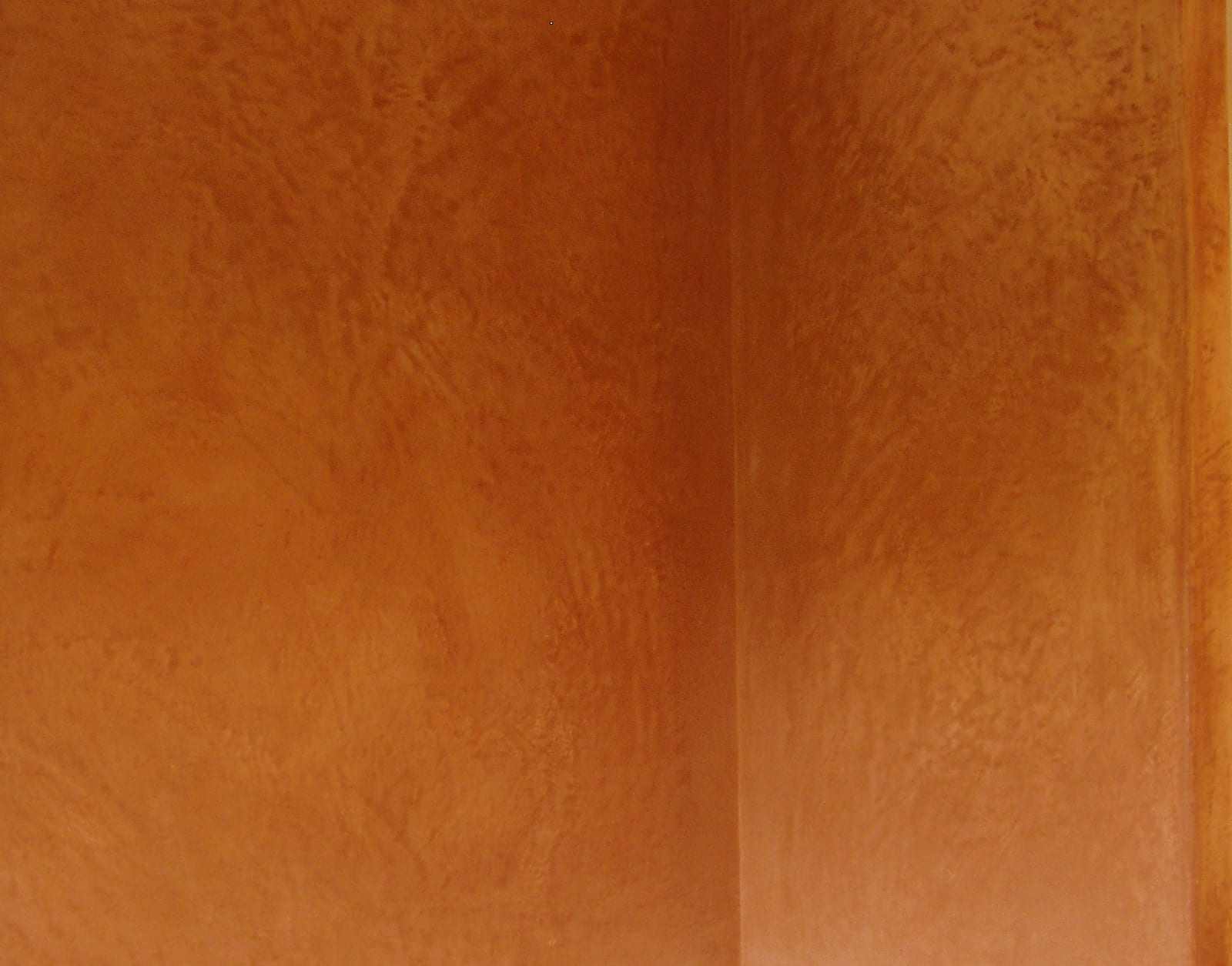 Warm terracotta clay plaster wall turning an internal corner, mottled trowel movement across a flat matte surface