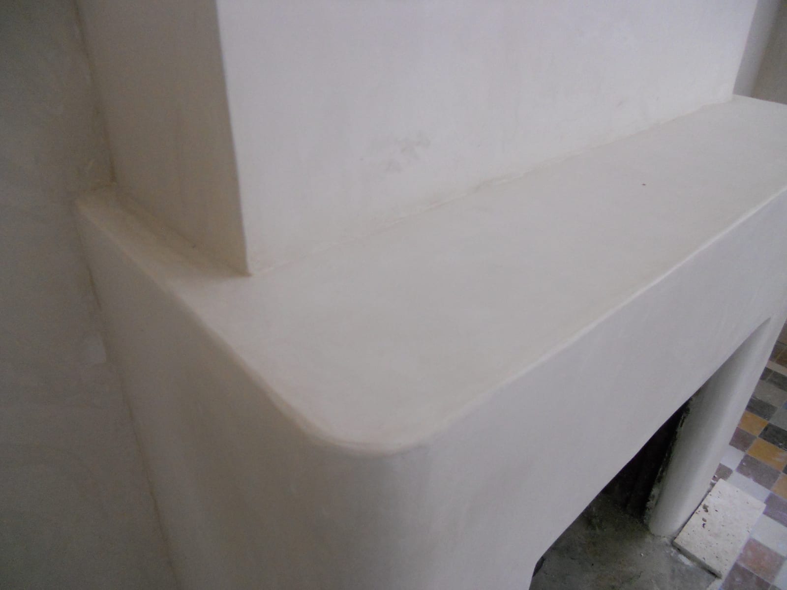 Tadelakt-finished fireplace surround in warm cream, edges softly rounded with no visible joint or seam